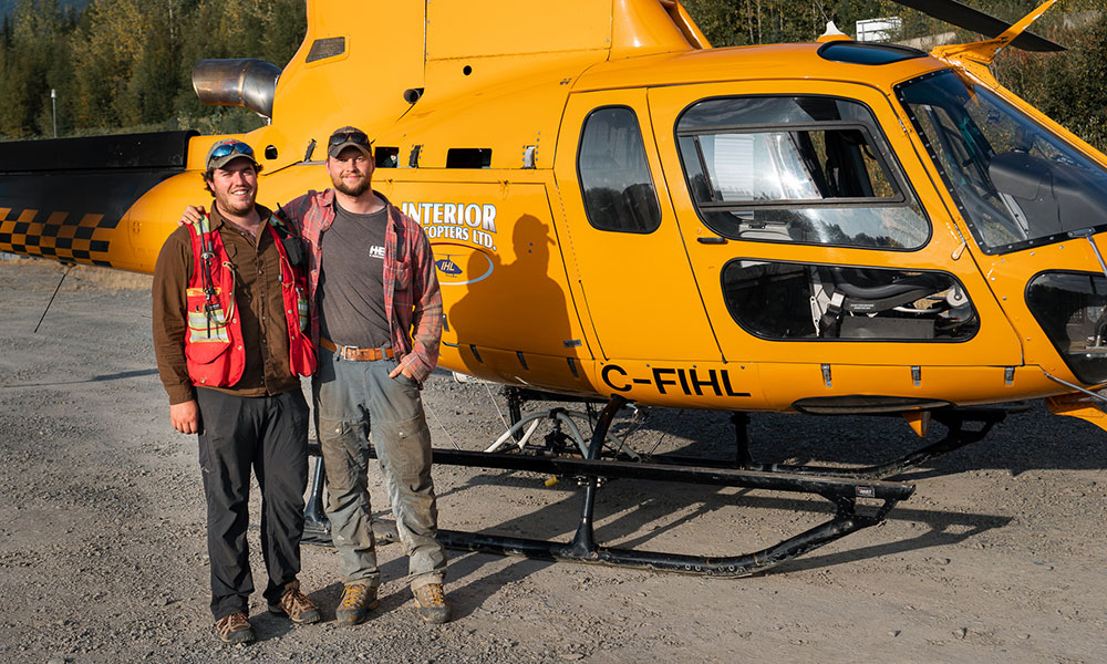 UBCO alumni Cole Evans and Dylan Hunko in front of the helicopter that will take them into the remote Canadian wilderness.